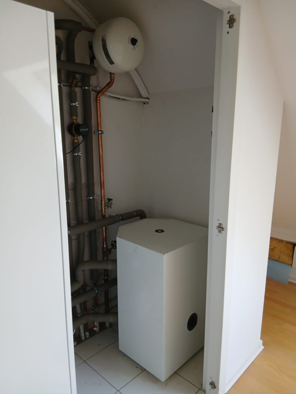 Kleiner Technikraum mit Wärmespeicher, Verrohrung, Ausdehnungsgefäß und Kupferleitungen.